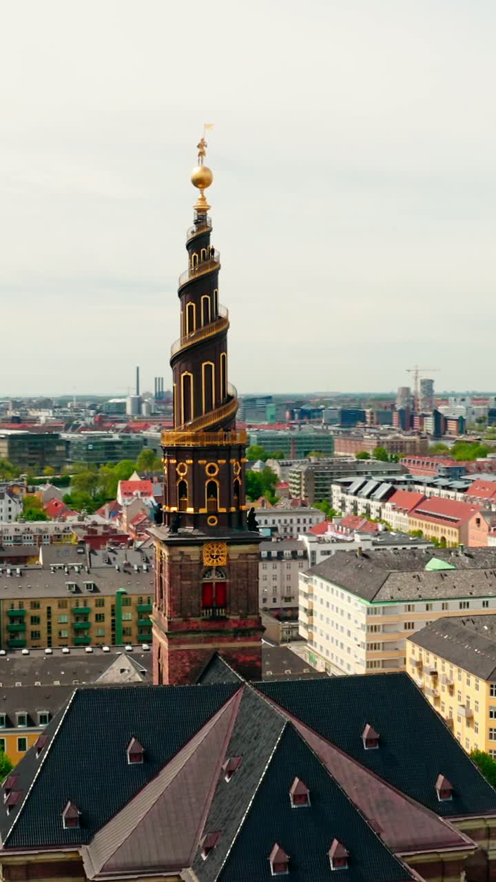 Vertical aerial shot orbiting the Church of Our Saviour’s spiral tower, surrounded by the colorful cityscape of Denmark