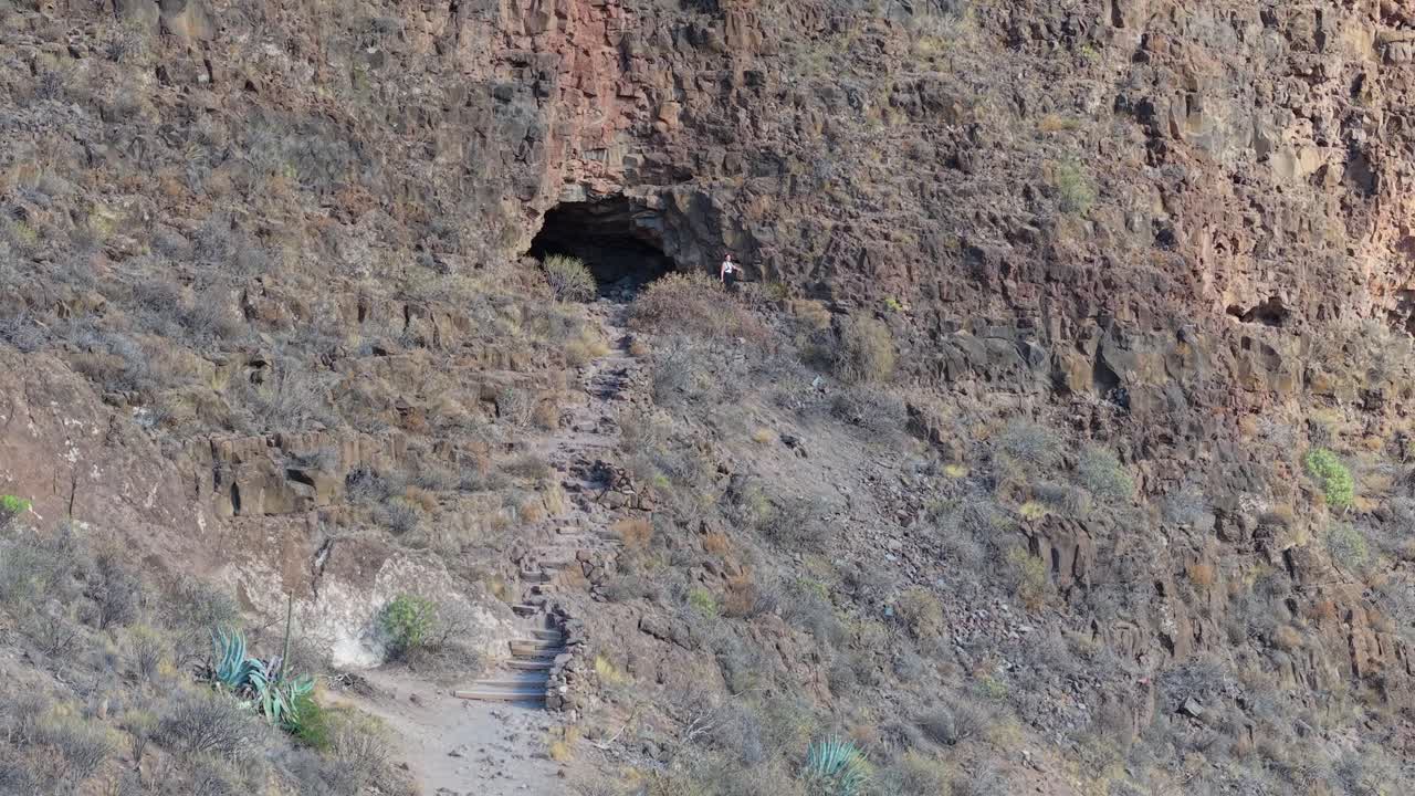 Fortezza di Ansite: turista che cammina su un sentiero di montagna verso l'ingresso di una grotta sull'isola di Gran Canaria