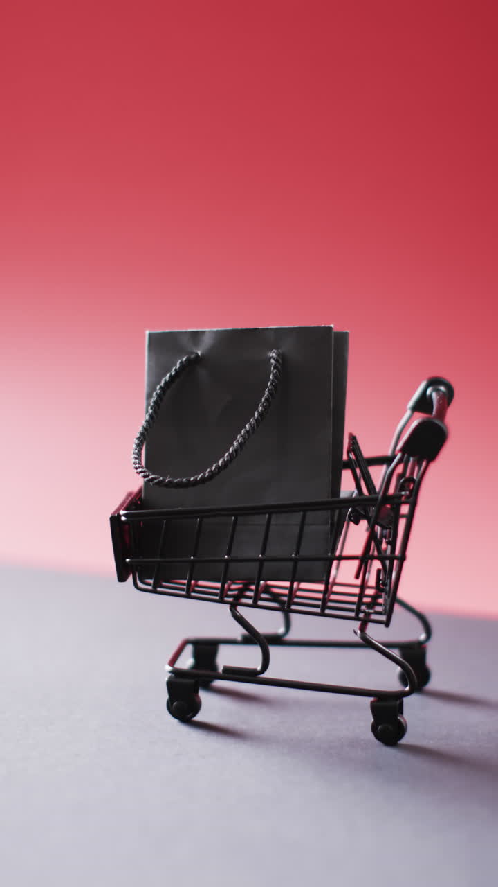 Vertical video of black gift bag in shopping trolley with copy space on red background