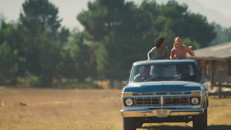 two women standing in back of pick up truck as friends enjoy road trip to countryside cabin