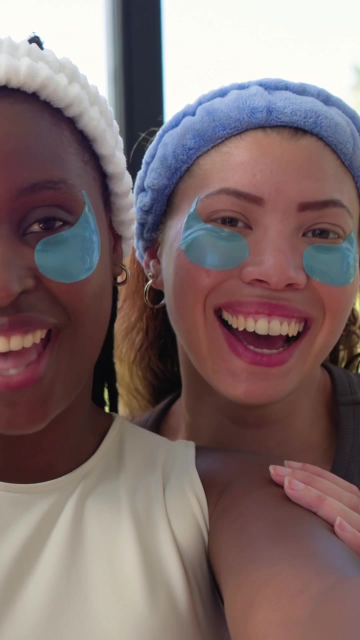 Vertical video: Smiling two women reaching to record selfie leaning close at home with eye patches