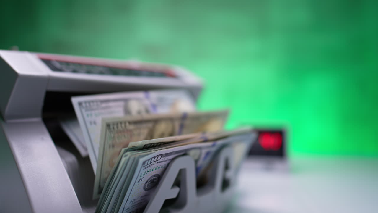Working cash counting machine with rotating blades. A stack of one hundred dollar bills is counted in equipment. Close up.