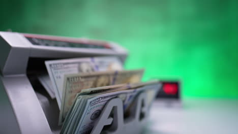 working cash counting machine with rotating blades. a stack of one hundred dollar bills is counted in equipment. close up.