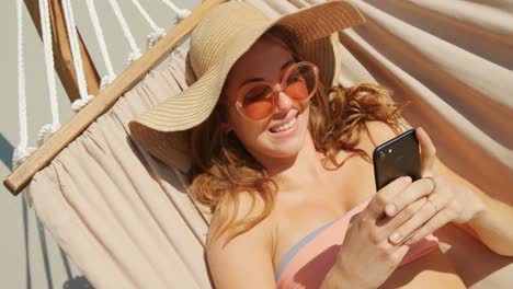 Vista-De-ángulo-Alto-De-Una-Mujer-Caucásica-Usando-Un-Teléfono-Móvil-En-Una-Hamaca-En-La-Playa-4k