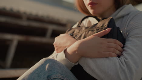 close-up of a young woman holding her bag closely with sunlight casting warm reflections on her hands and jeans, creating a sense of solitude and introspection