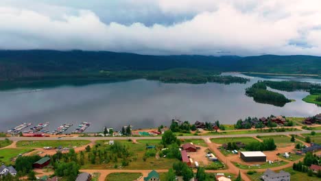 Aerial-Drone-View-of-Beautiful-Clear-Mountain-Lake-with-Cars-Driving-on-Highway-Road-in-Grand-Lake-Colorado-with-Boat-Docks-and-Lush-Pine-Trees-next-to-Shadow-Mountain-Reservoir