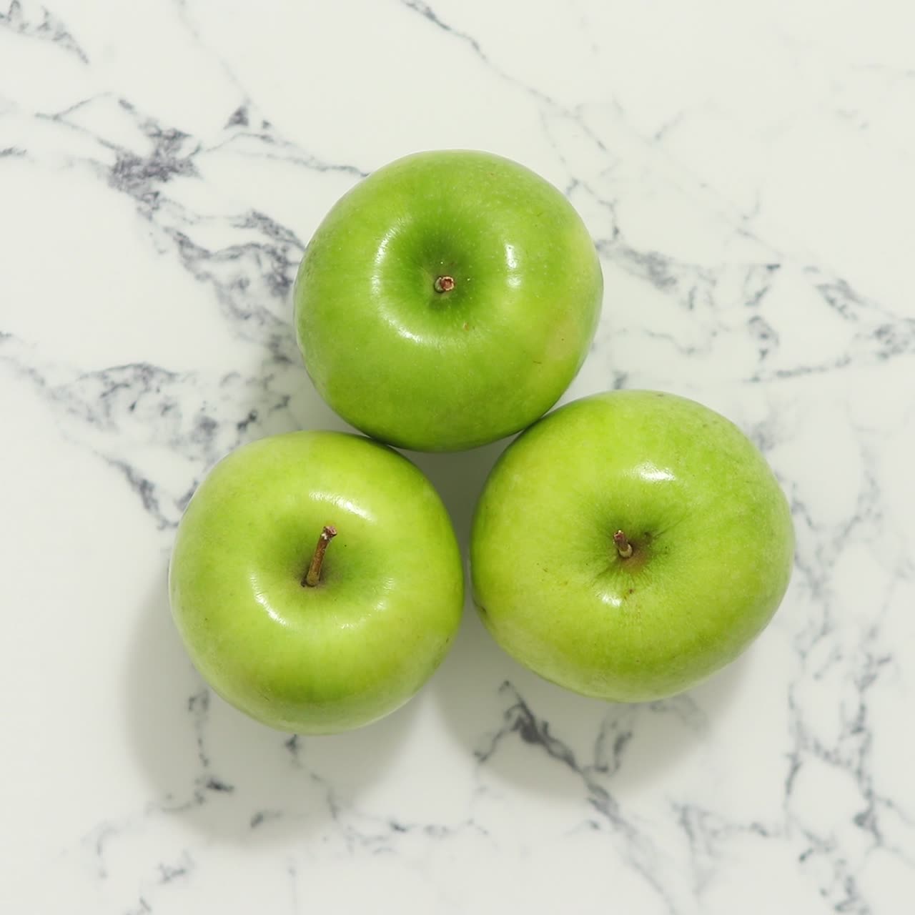 tres manzanas verdes frescas colocadas sobre una mesa de mármol blanco
