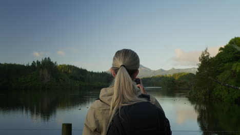 fotógrafa rubia que toma una foto de paisajes naturales de un lago y un volcán lejano