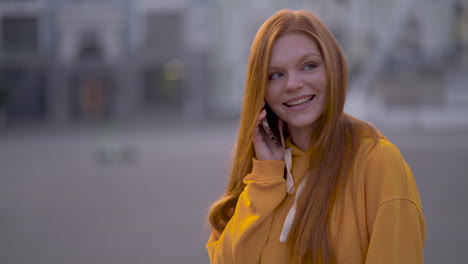 joven y bonita mujer pelirroja hablando por teléfono al aire libre