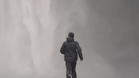 man in outdoor gear, seen from behind, running purposefully towards the powerful mist of skógafoss waterfall in iceland
