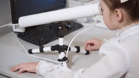 chica mirando a través de un telescopio a una computadora