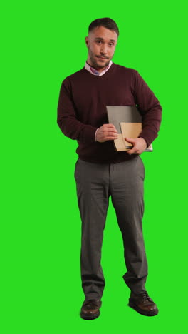 man in a sweater and pants holding files in front of a green screen