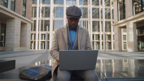 stylish african american businessman working on laptop in city