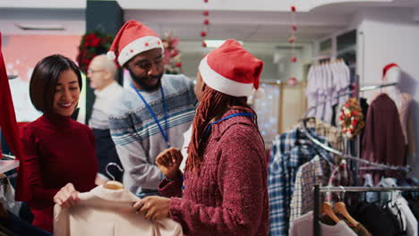 tracking shot of employee bringing elegant blazers for customer to try on while colleague helps her with information. retail assistants presenting garments to client in christmas ornate fashion shop