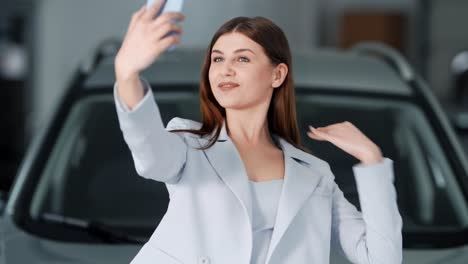 Beautiful-stylish-dressed-young-woman-takes-pictures-of-herself-on-a-smartphone-on-the-background-of-the-car