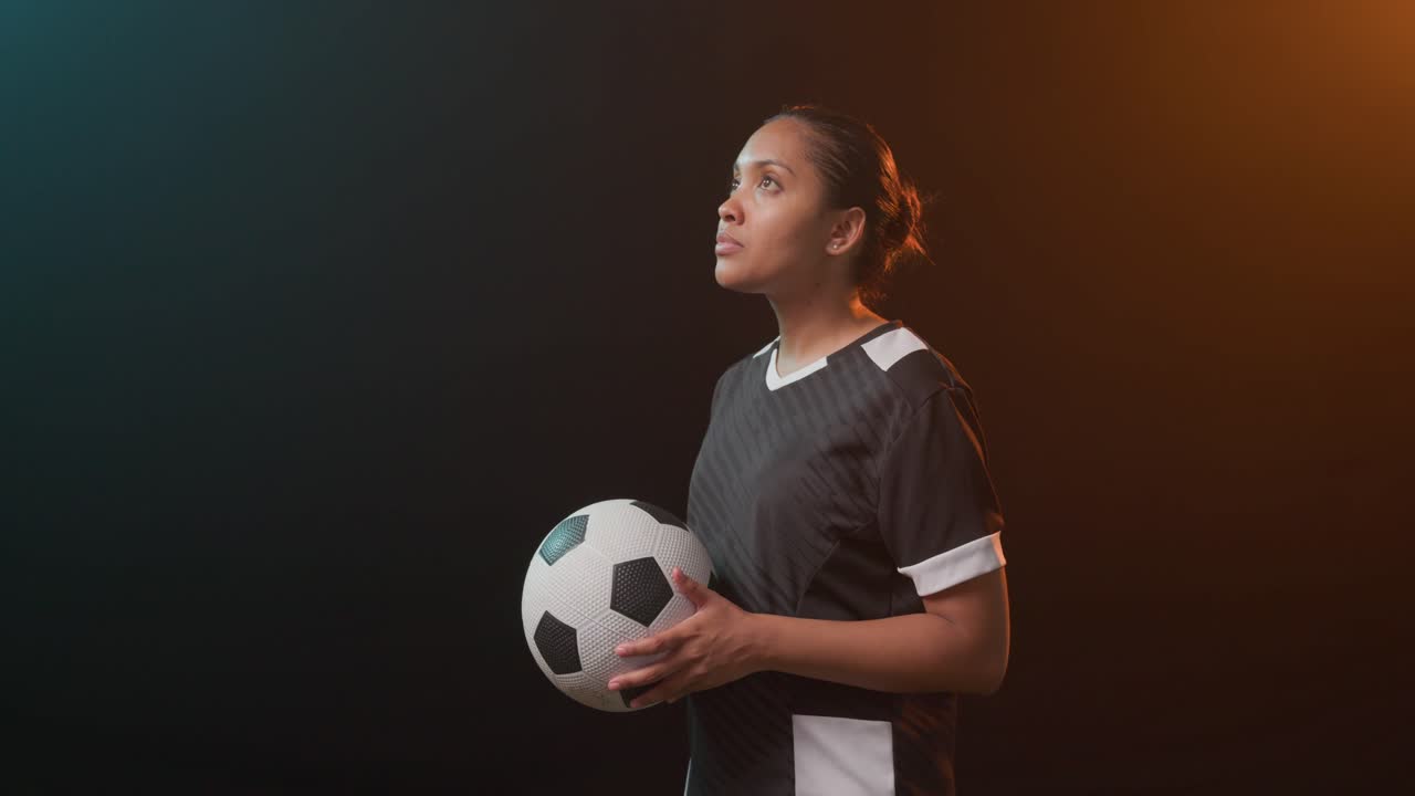 Atleta donna che regola la presa sul pallone da calcio, con lo sguardo rivolto in avanti e sorridendo per il branding sportivo