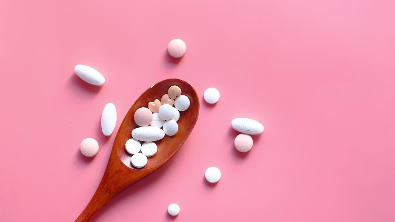 Assorted Pills in a Wooden Spoon on Pink Background