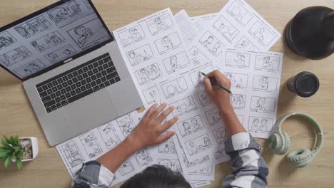 close up top view of asian male artist drawing storyboard for the film on the table with a laptop and headphones in the studio