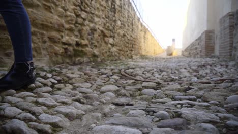 Toma-En-Cámara-Lenta-De-Los-Pies-De-Una-Persona-Caminando-Sobre-Un-Suelo-De-Guijarros-En-Una-Calle-Rural-Romana