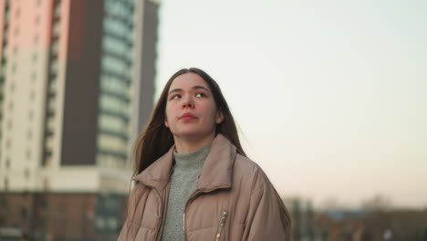 a close-up front shot of a young girl wearing a peach jacket and a grey inner sweater, captured while walking through an urban park. the shot focuses on her upper body and contemplative expression