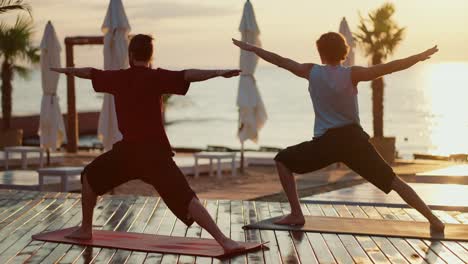 meditation of two guys who stand on a wooden floor on the beach and stretch their arms to the sides. yoga and zen style