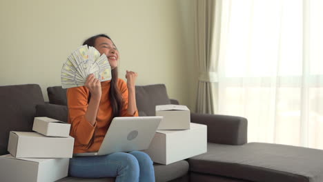 exultant asian woman show dollar money cash with computer notebook