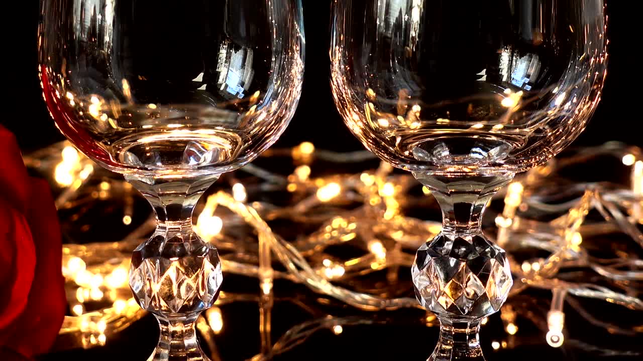 Copas de vino y rosa sobre el fondo de guirnaldas brillantes