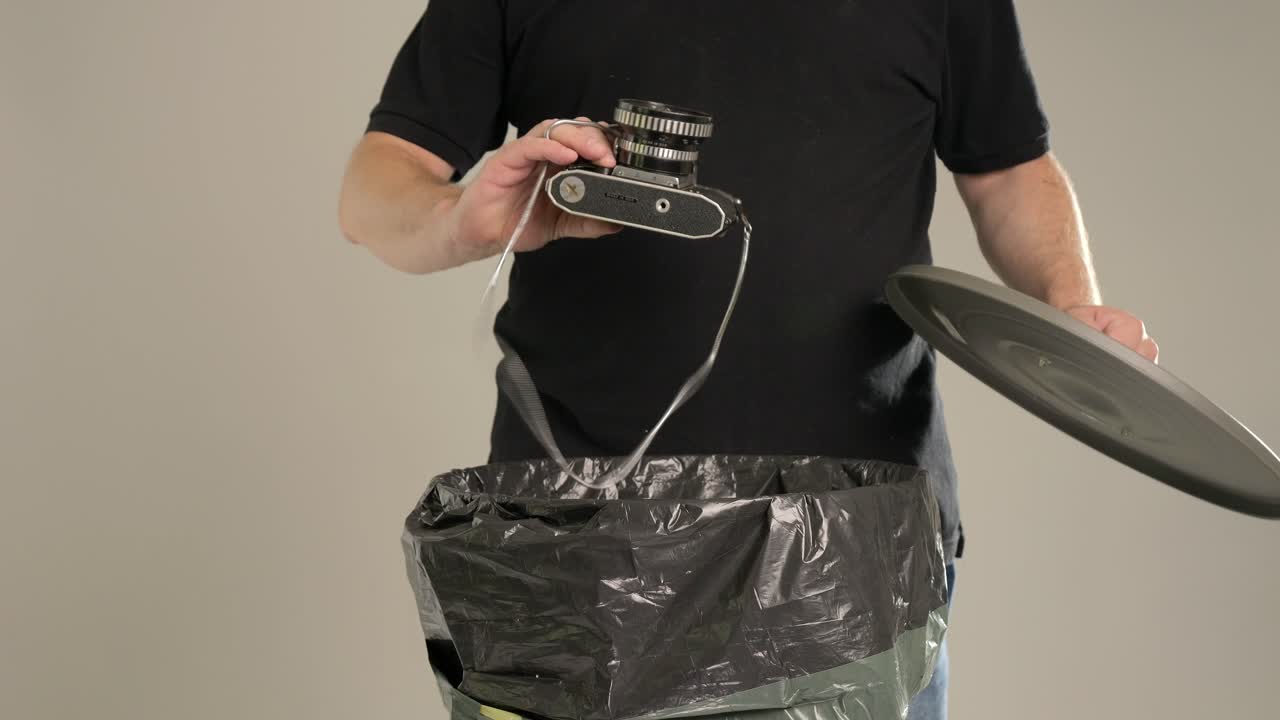 한 남자가 오래된 카메라를 쓰레기통에 던지고 있다.