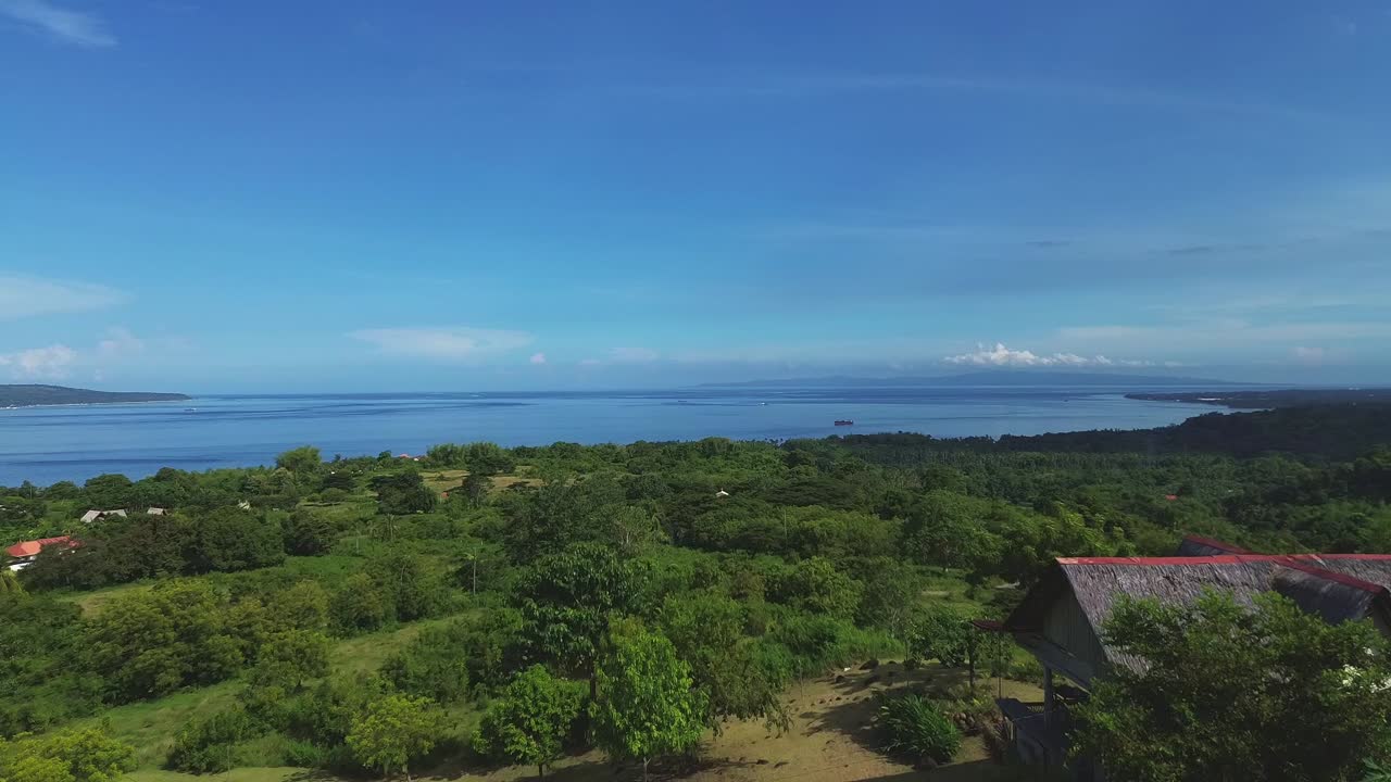 FPV drone flyover from a native house to the expansive view of lush green mango plantation heading to the distant horizon of blue sea and sky in San Jose, Negros Oriental, Philippines