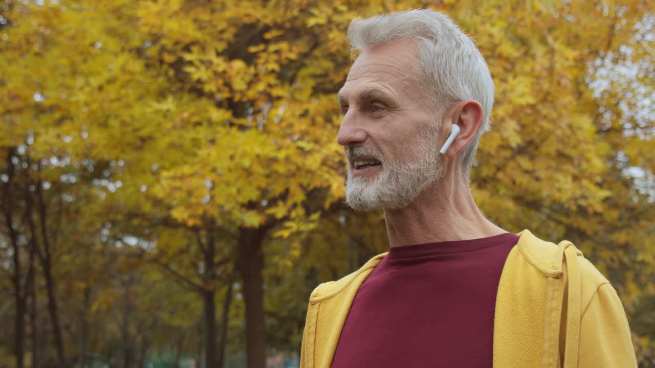 pensionista moderno hablando por teléfono, usando auriculares inalámbricos al aire libre, tecnología