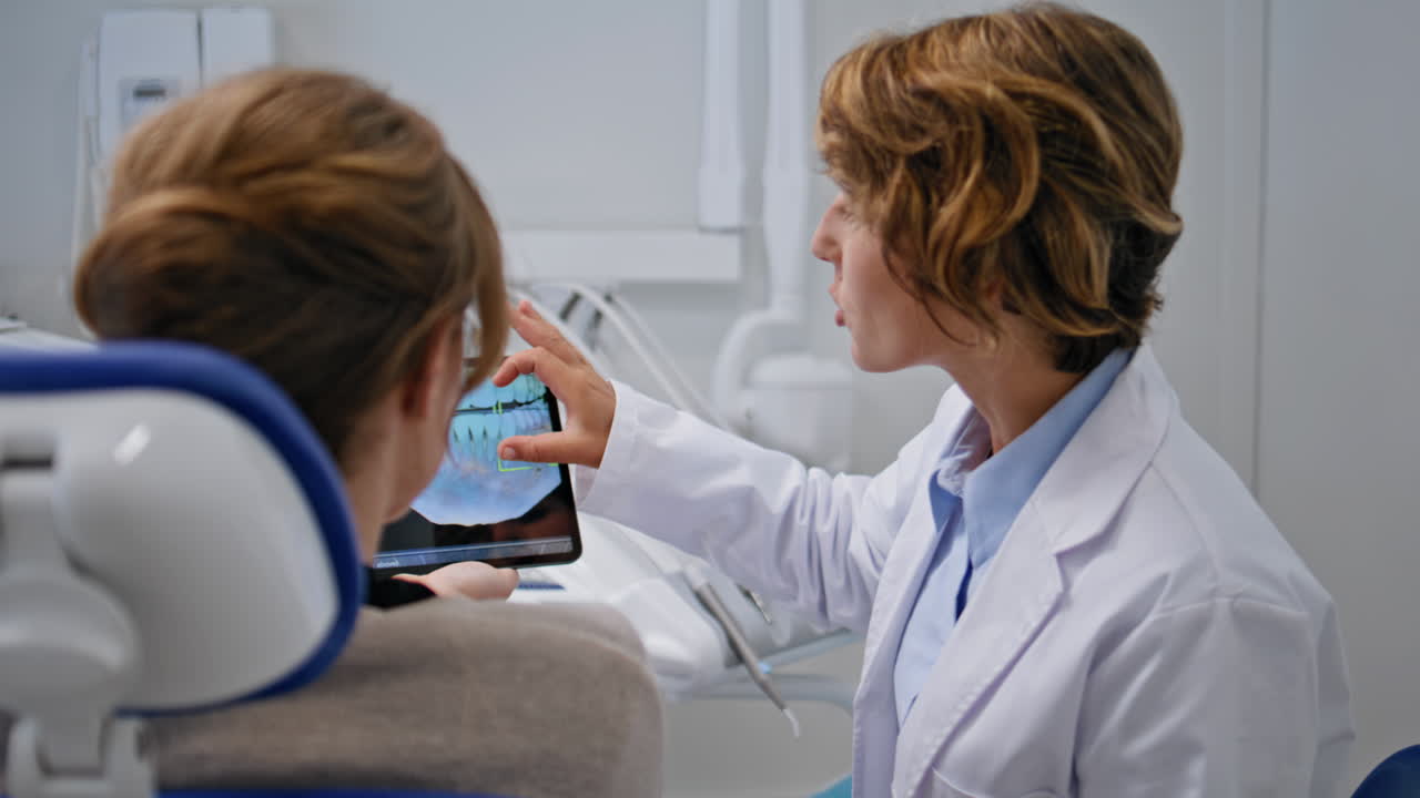 Woman orthodontist explaining x-ray using tablet in stomatology clinic closeup