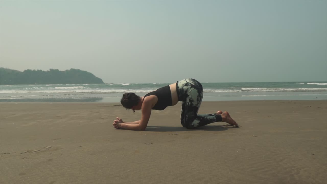 práctica de yoga arrodillada en una espectacular playa de arena negra con olas de fondo