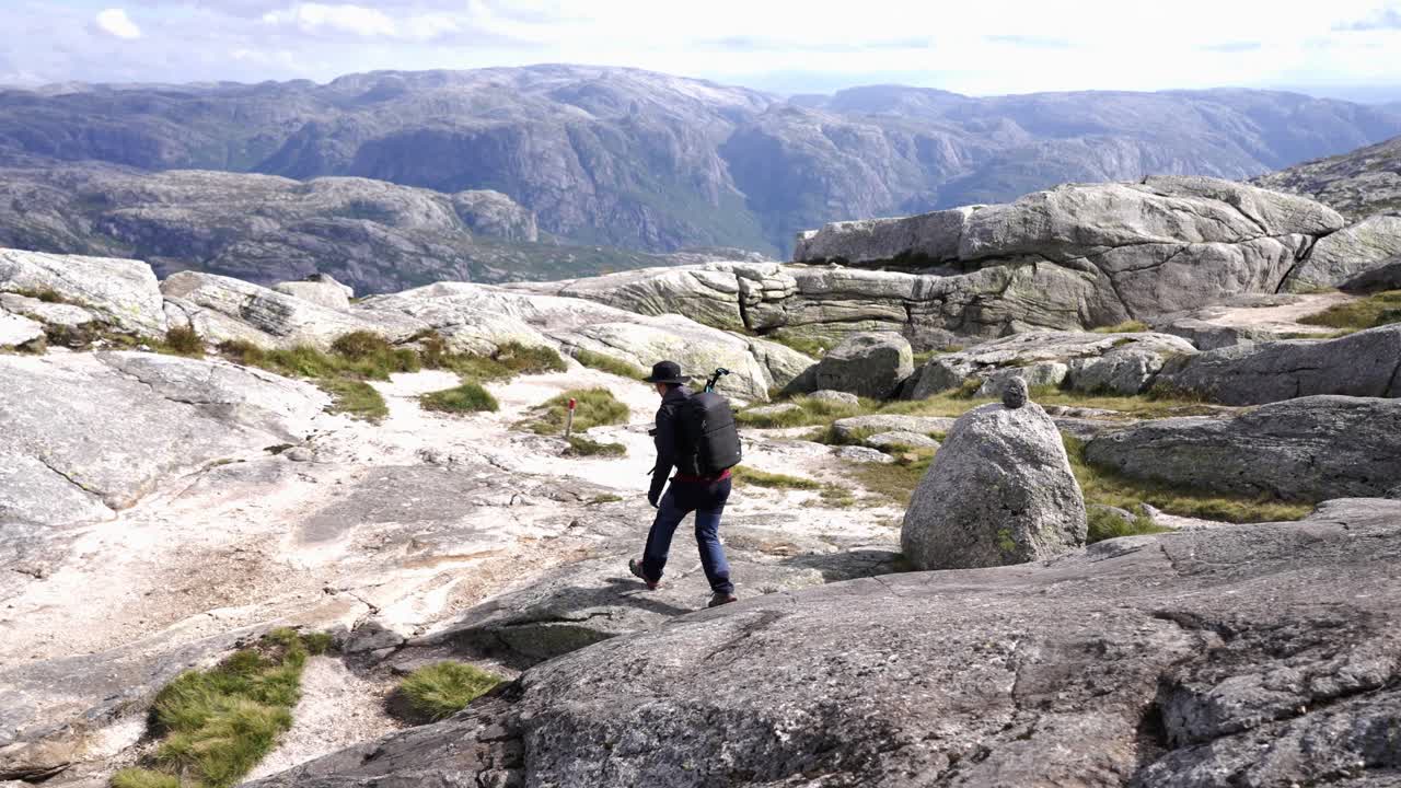 A hiker walks across rocky terrain with breathtaking views of the Norwegian mountains