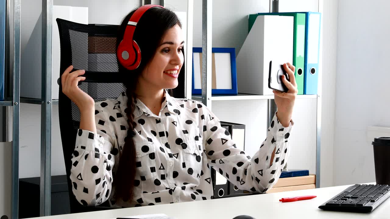 mujer de negocios con auriculares rojos grabando video en un teléfono inteligente en una oficina moderna