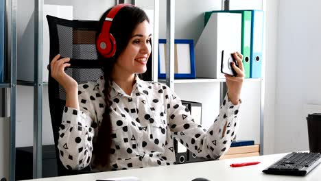 mujer de negocios con auriculares rojos grabando video en un teléfono inteligente en una oficina moderna