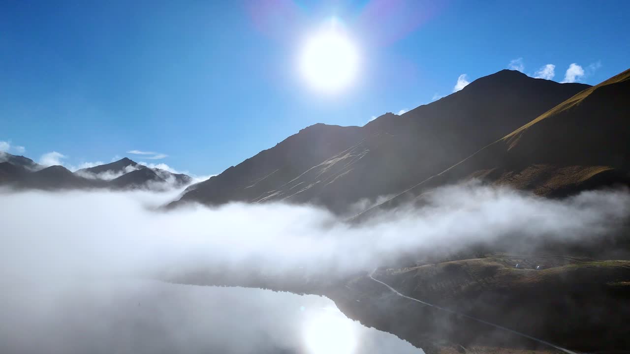 A serene view of fog rolling over Moke Lake, Queenstown, under bright sunlight and clear blue skies
