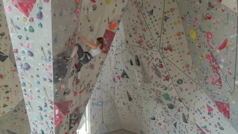 aerial: flying near an athletic woman indoor lead climbing up a difficult route.