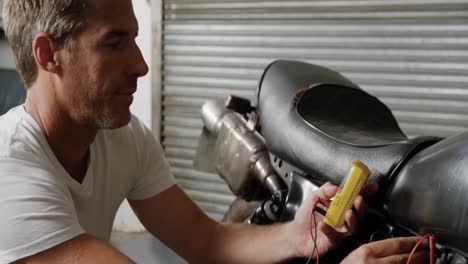 Male-mechanic-checking-battery-of-motorbike-in-repair-garage-4k
