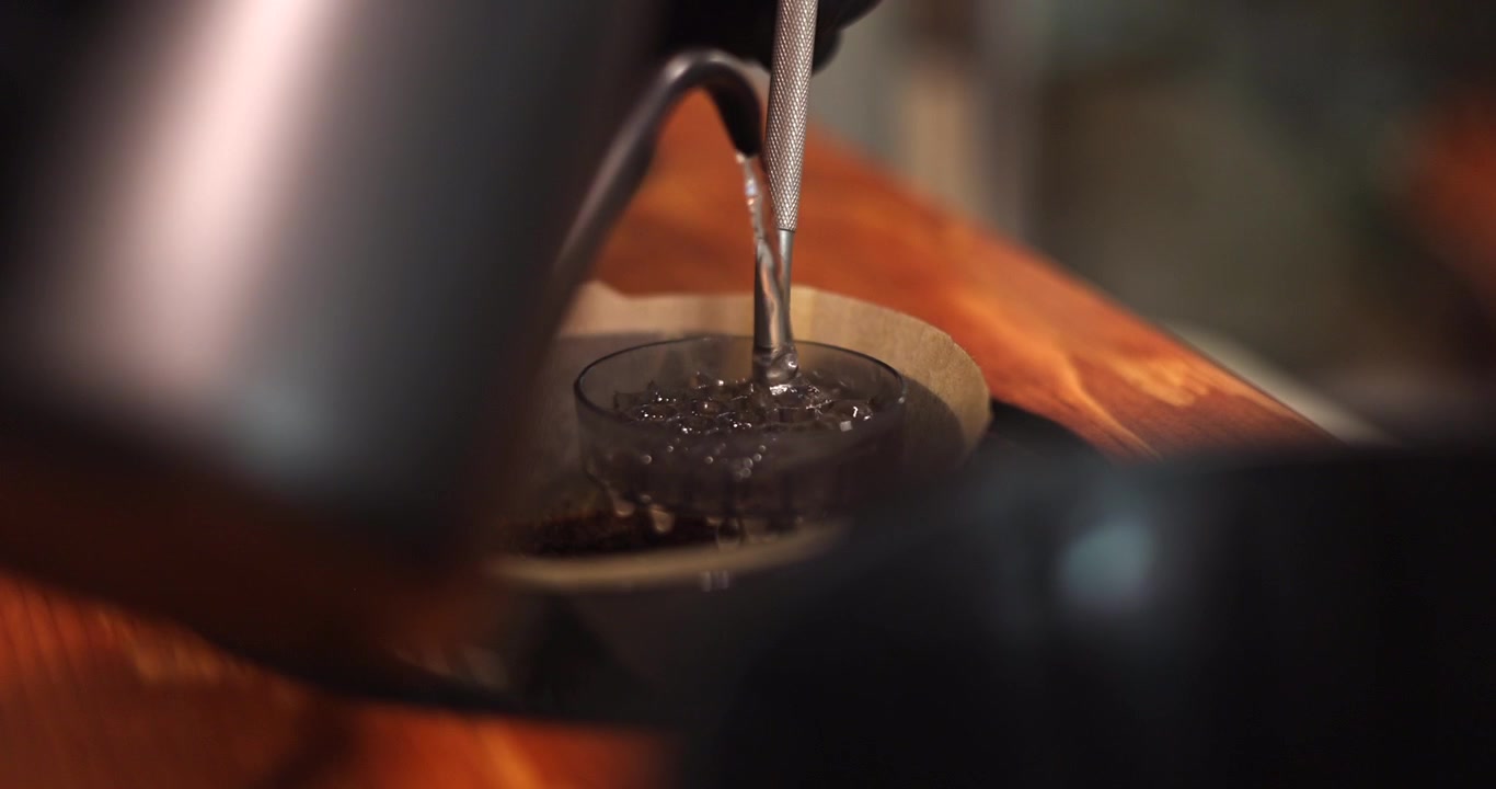 Gooseneck kettle pours hot water through a dispersion screen during pour over coffee brewing, detailed medium closeup, slow motion