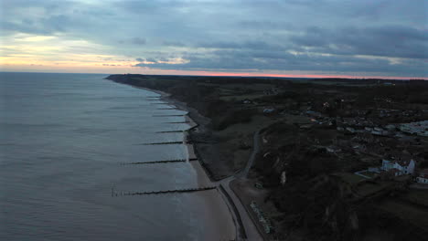 Aerial-flight-high-over-Overstrained-in-Norfolk-at-sunrise-with-a-lighthouse-flashing-and-fast-moving-clouds