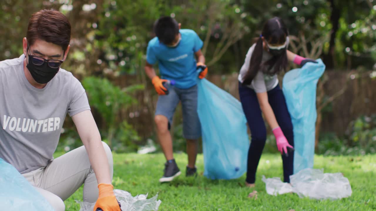 Genitori, figlio e figlia asiatici che indossano mascherine, che tengono sacchi per i rifiuti e raccolgono rifiuti di plastica.