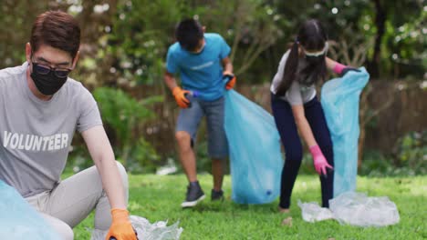 Asian-parents,-son-and-daughter-wearing-face-masks-holding-refuse-sacks-collecting-plastic-waste