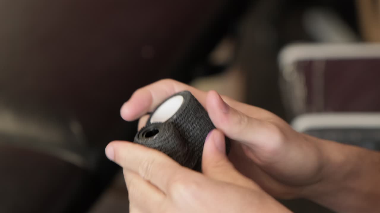 Close up of tattoo artist hands preparing tattoo gun by ripping grip tape.