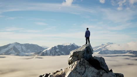 adventurous male hiker standing on dramatic rocky cliff, low clouds and snowy mountain landscape