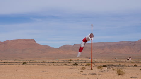 Shot-of-an-isolated-windsock-blowing-gently-in-the-wind-at-a-desert-airfield,-high-mountains-in-the-background