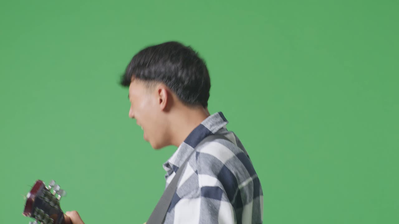 녹색 스크린 배경에 록 음악과 함께 기타를 연주하는 젊은 아시아 십대 소년의 가까운 측면 시각