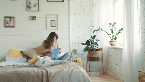 une mère au ventre joyeux à la recherche de vêtements pour bébé. une femme enceinte heureuse assise dans la chambre.