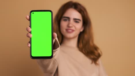 woman showing cellphone with green screen in studio