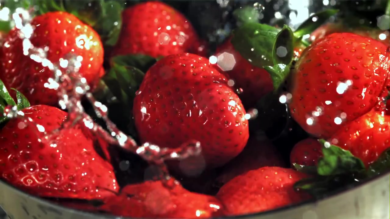 Fragole rosse fresche che vengono lavate con acqua che schizza.