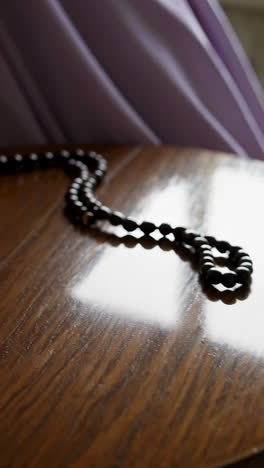 rosary on wooden table with purple fabric